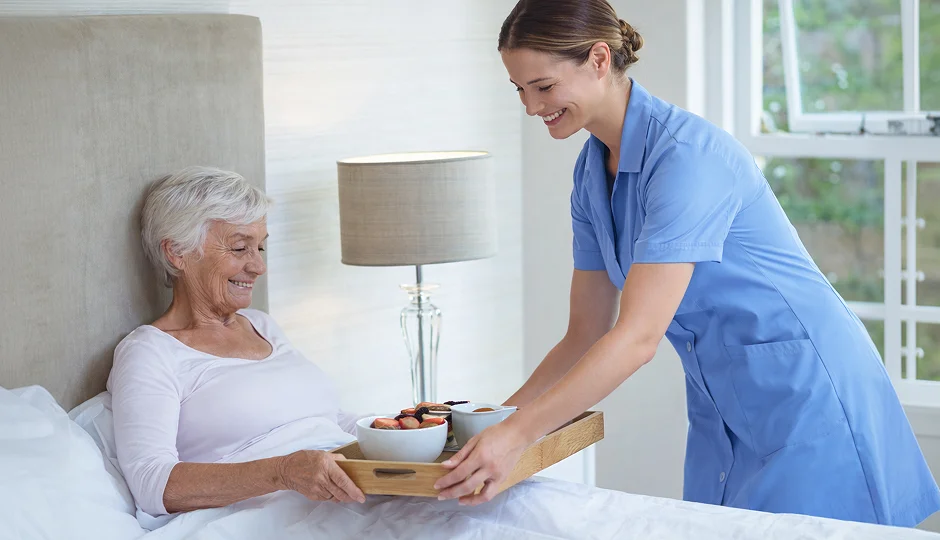Caregiver serving breakfast to a senior woman in bed