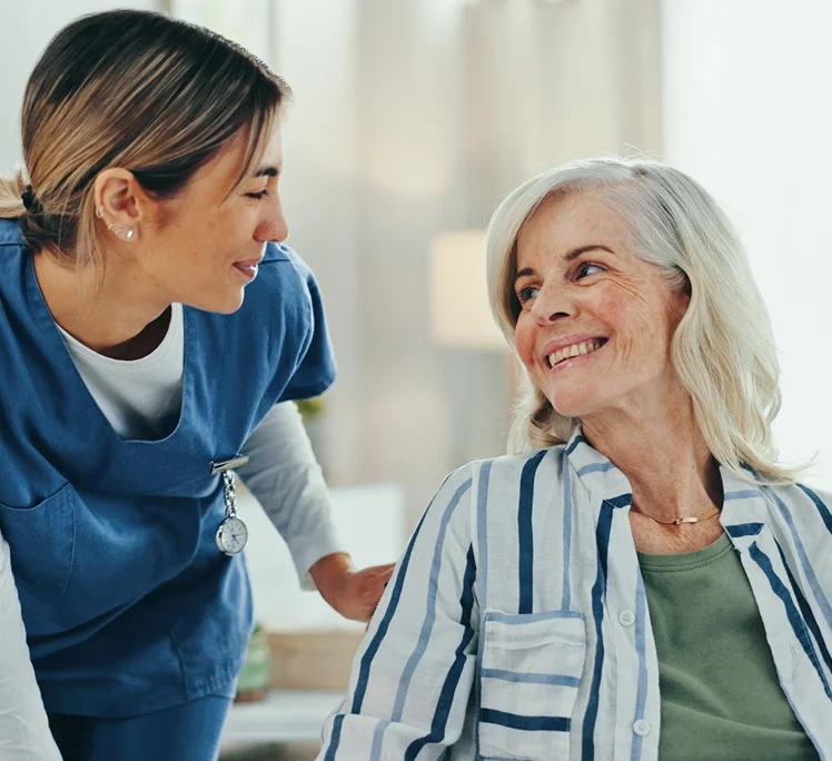 Caregiver smiling and talking with a senior woman at home