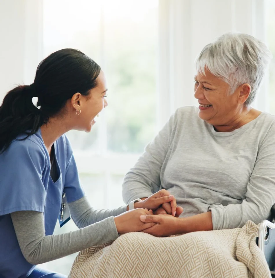 Social worker holding an older woman's hands during a home visit.