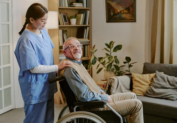 Clinician supporting an older man in a wheelchair at home.