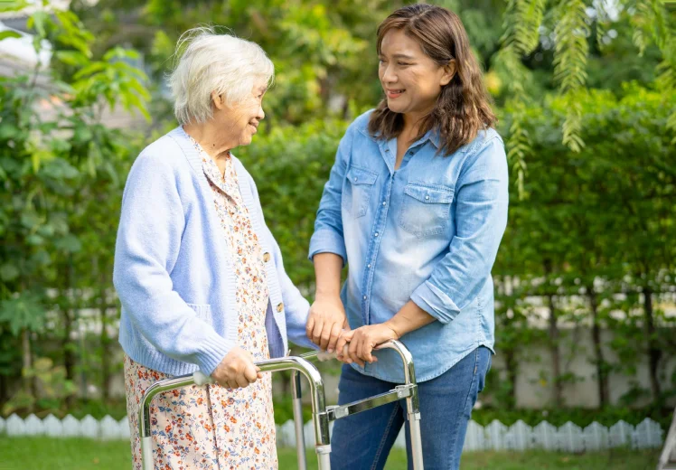 Caregiver walking outdoors with an older woman using a walker.