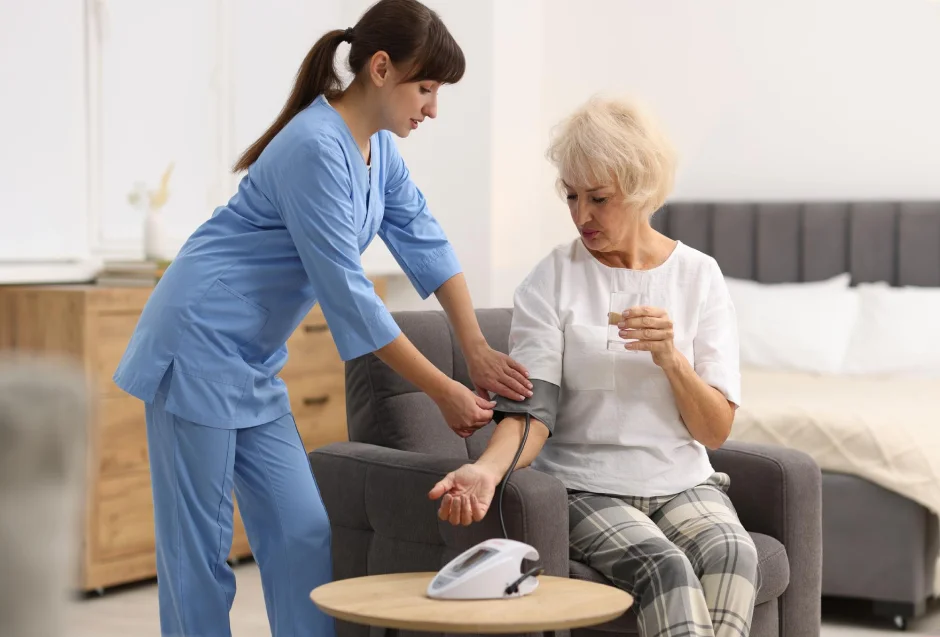 Nurse helping an older woman stand safely from a sofa.