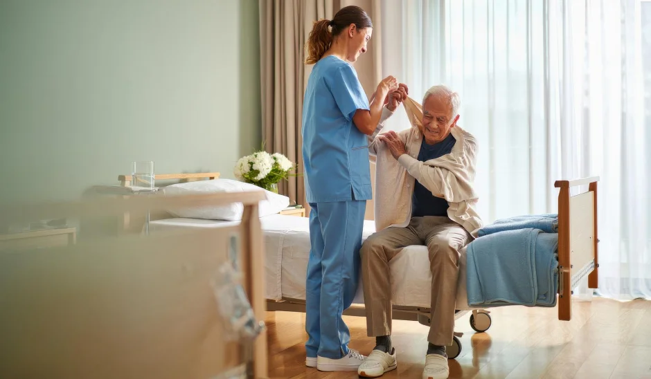 Aide assisting an older man to stand from bed.