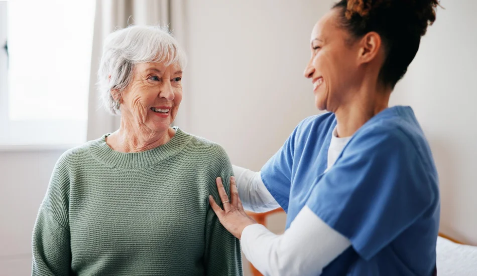 Nurse supporting a smiling older woman during a home visit.