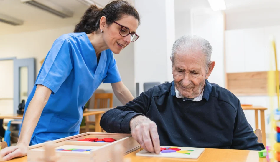 Therapist guiding an older man through a tabletop activity.