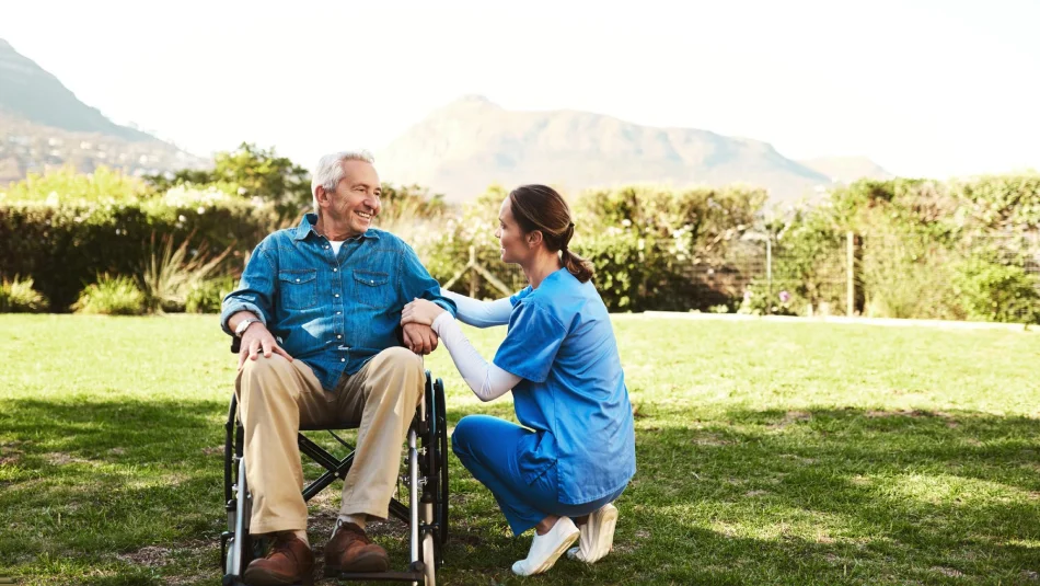 Aide talking with an older man in a wheelchair outdoors.