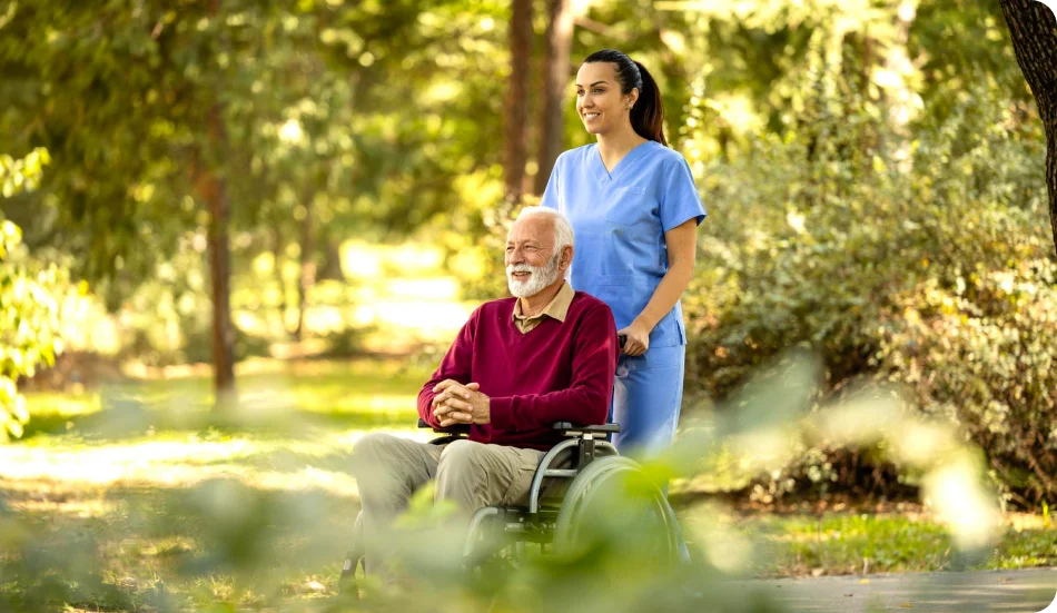 Caregiver pushing a senior man in a wheelchair through a park