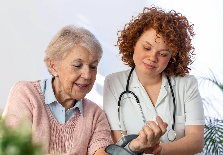 Caregiver checking a senior woman's blood pressure during a home visit