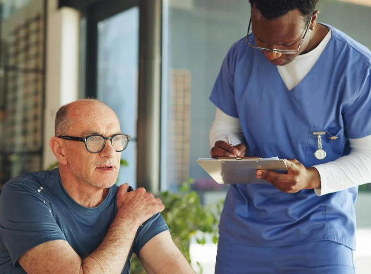 Caregiver taking notes while assessing a senior patient with shoulder pain